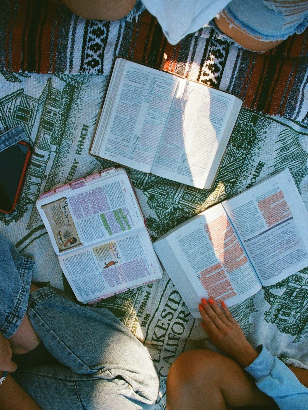 Three open Bibles laid out on a blanket, seen from above, as a group reads together
